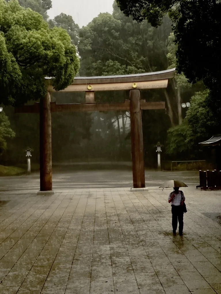 A lone figure with an umbrella crossing a shrine courtyard in heavy rain